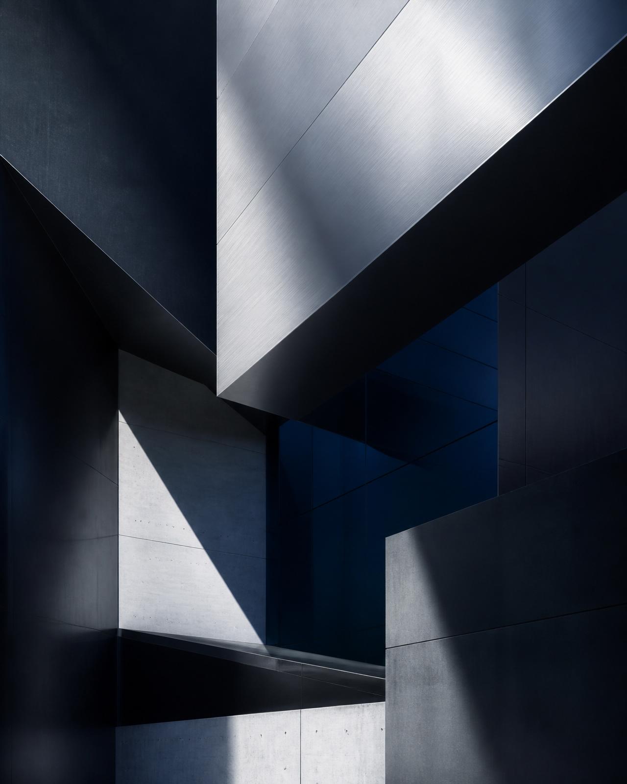 Abstrakte, moderne Arbeitsumgebung eines Berufsgeheimnisträgers: geometrische Anthrazit- und Stahlflächen mit tiefblauem Glaslicht als Sinnbild einer eigenen, sicheren KI-Workstation im Haus
